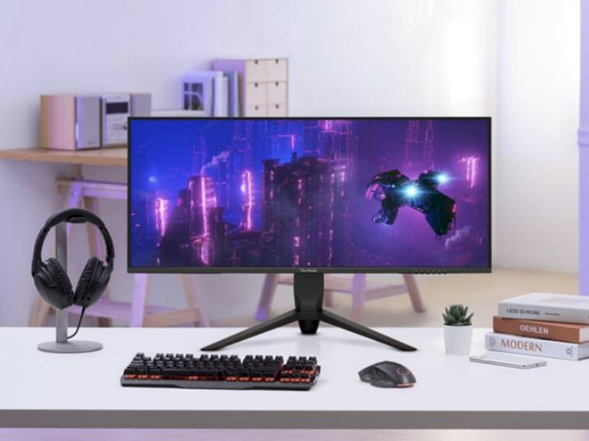 Sürükleyici oyun deneyimi ve yaratıcı çalışmalar için neon siberpunk bir sahne sergileyen ultra geniş monitörlü modern masa düzeni.